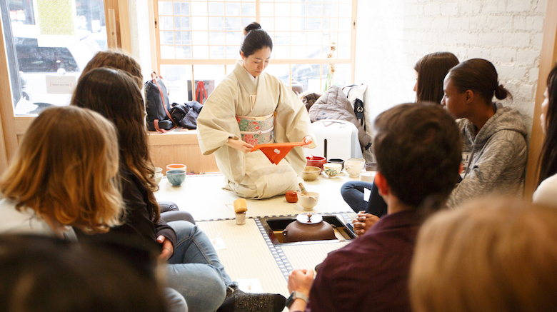 Japanese woman preparing tea, seated with students.
